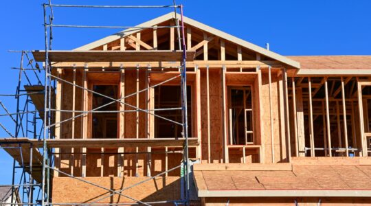 Upper portion of a multistory workforce housing building under construction, with wood framing and scaffolding visible.
