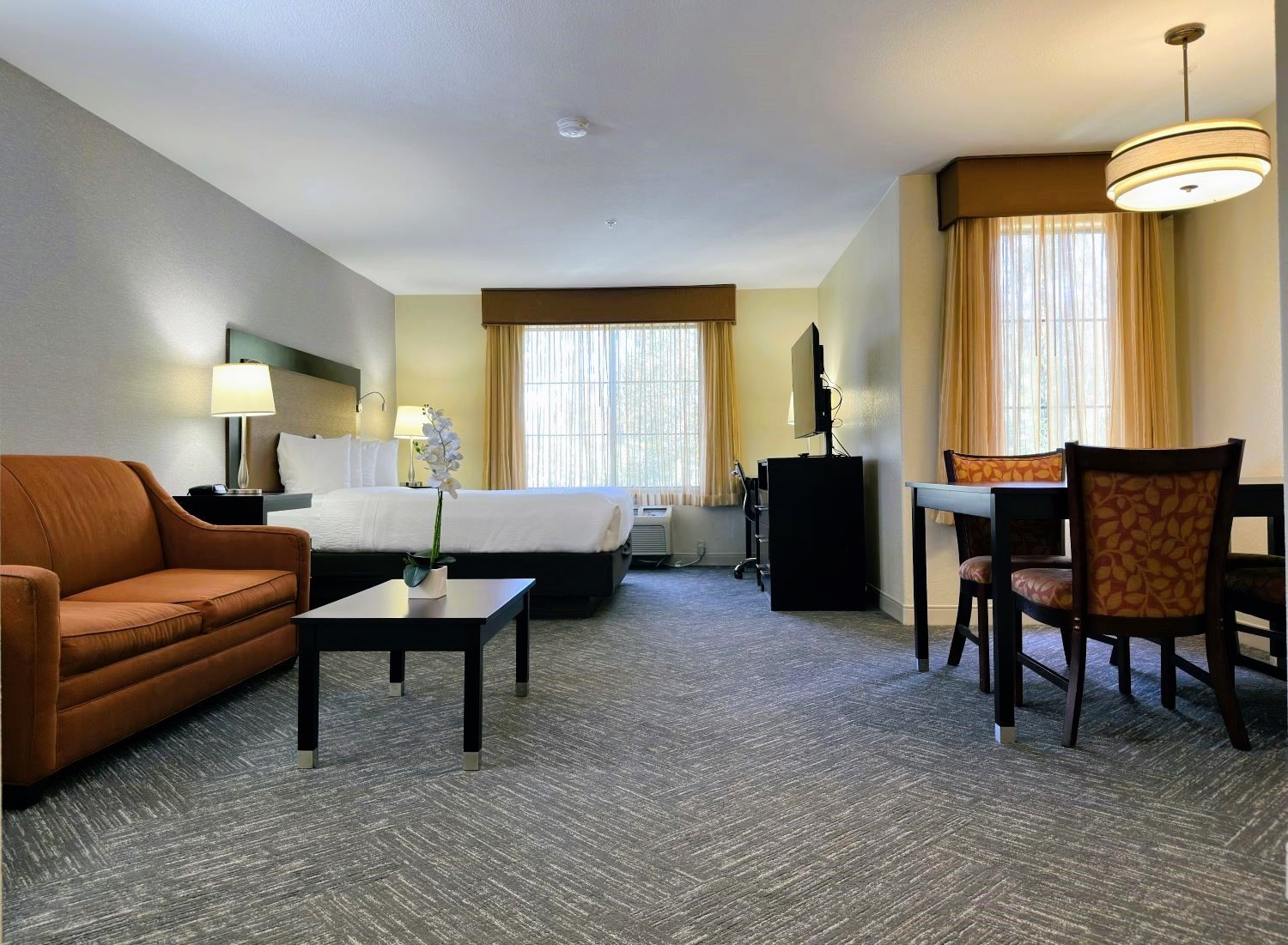 Renovated king guest room at the Best Western Escondido Hotel featuring a king bed, loveseat, coffee table, dining set, and updated finishes.