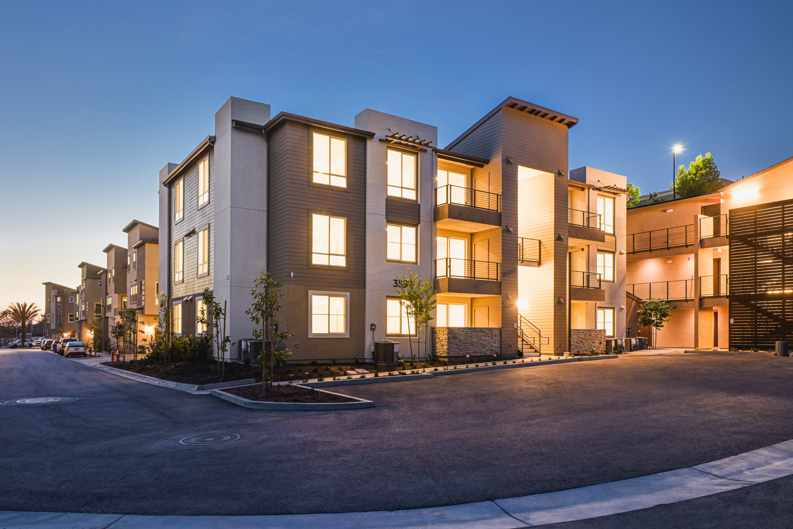 La Costa Family Apartments exterior at dusk in Carlsbad, showing contemporary architecture, varied massing, and illuminated balconies