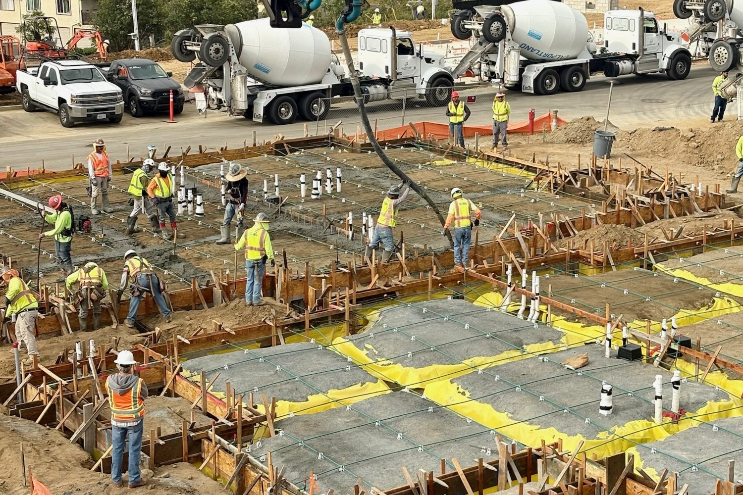 Construction crew placing concrete foundation with rebar grid and plumbing rough-ins during ground-up commercial development project.