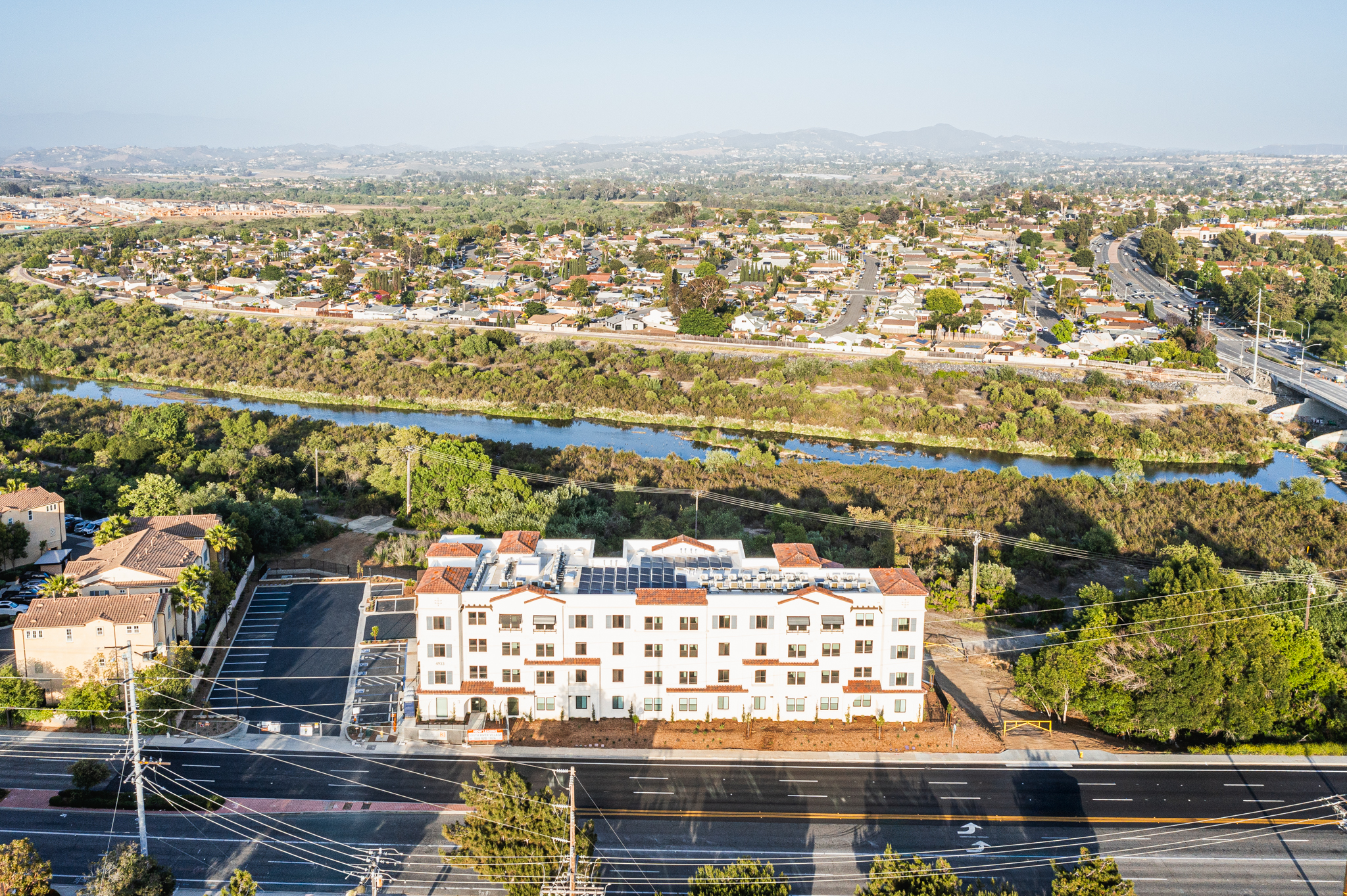 Birdseye view of the exterior of South River Village. This four-story Spanish Mission–style affordable housing community in Oceanside, CA features stucco walls, a tile roof, and landscaped surroundings.